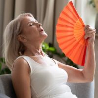 Mature women experiencing hot flashes, fanning herself to cool down. Click to learn more about our hot flash clinical research study.
